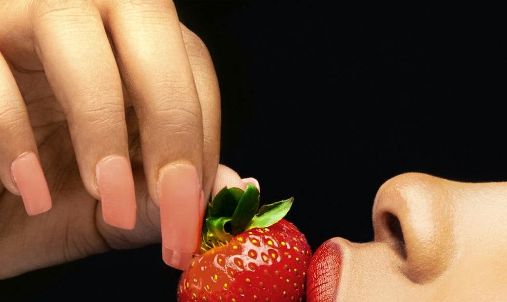 a close up shot of a woman with red lips eating a strawberry