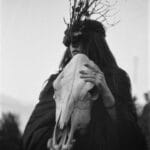 Black and white portrait of a shaman woman holding an animal skull, evoking a mystical and fantasy theme. 