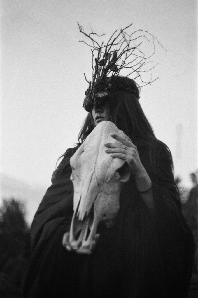 Black and white portrait of a shaman woman holding an animal skull, evoking a mystical and fantasy theme. 