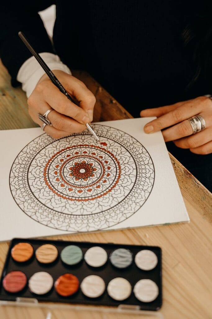 Close-up of hands painting a detailed mandala indoors, showcasing artistic creativity and precision. zen art